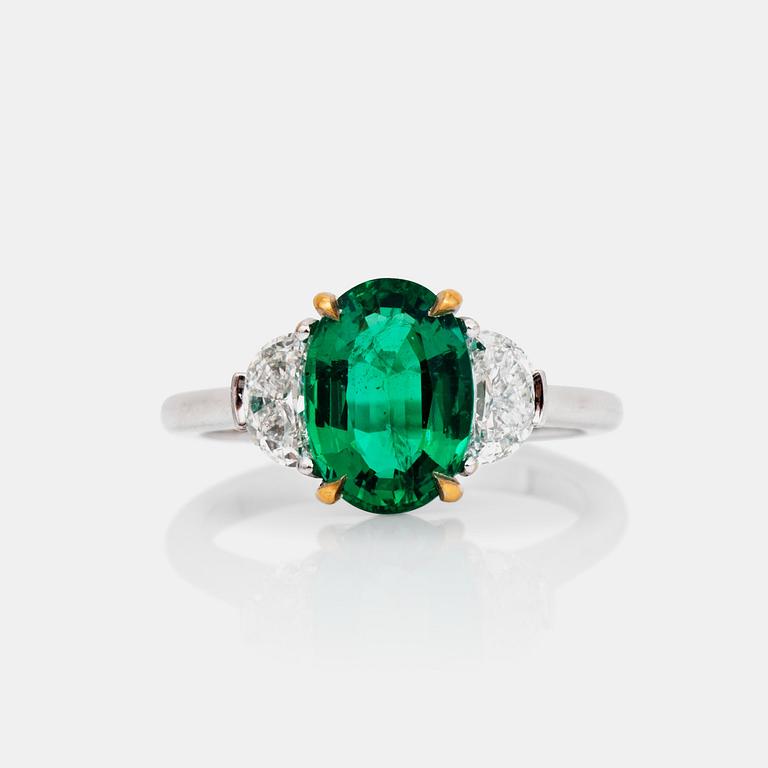 A 2.29ct oval-cut emerald ring. The emerald flanked by half moon shaped diamonds, total carat weight circa 0.81ct.