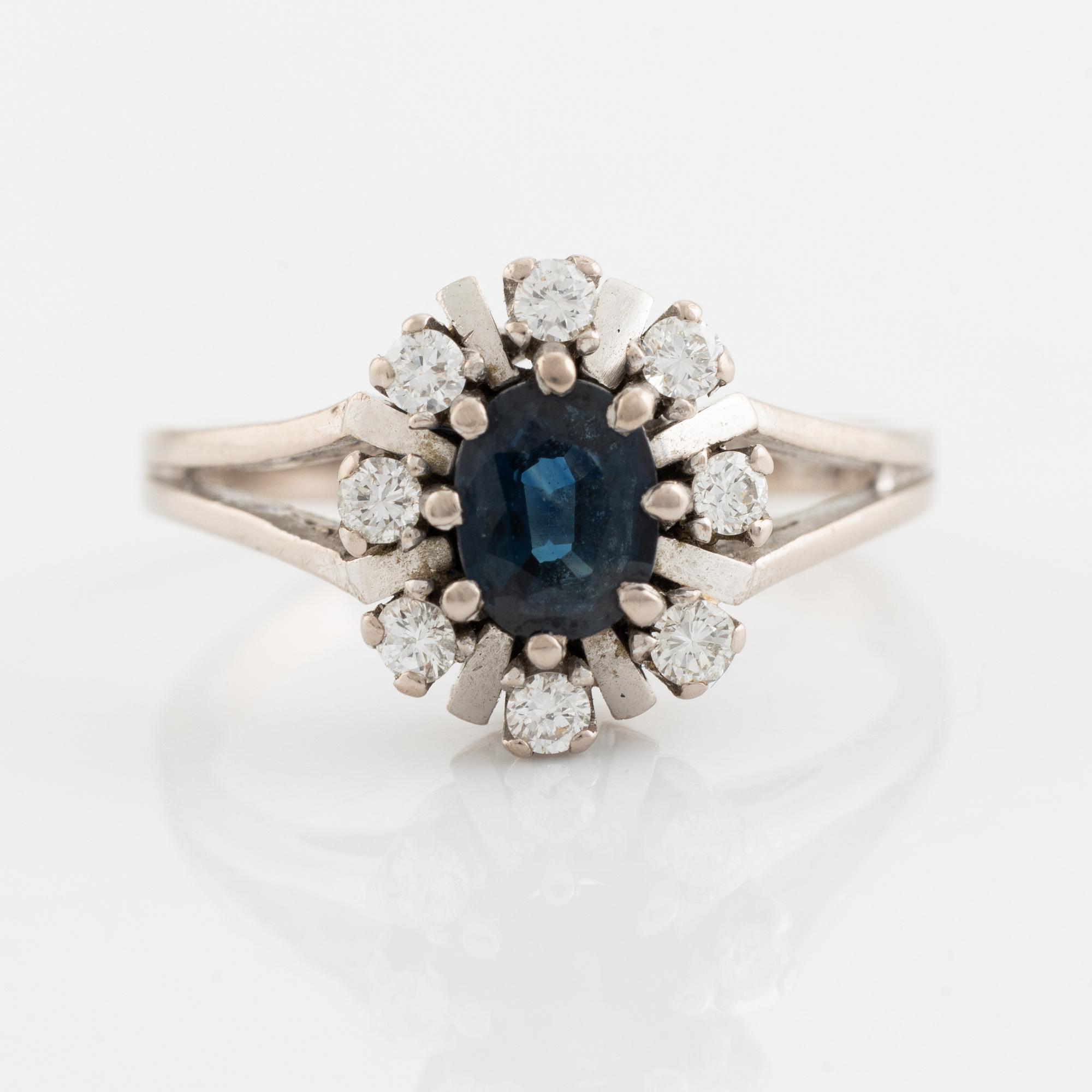 An 18K white gold ring set with a faceted sapphire and round brilliant-cut diamonds.