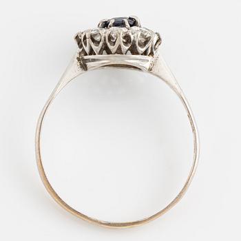 An 18K white gold ring set with a synthetic sapphire and round brilliant-cut diamonds.