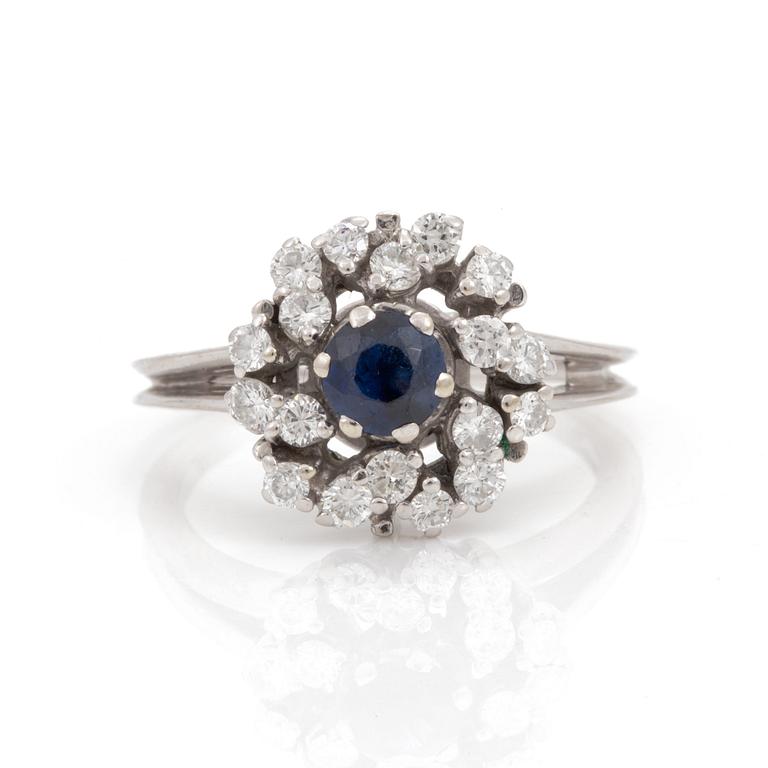 A ring set with a round, mixed-cut synthetic sapphire and round, brilliant-cut diamonds.