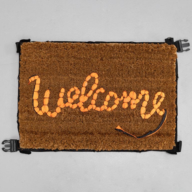 Banksy, "Welcome", Hand-stitched doormat using the fabric from life vests, 2019.