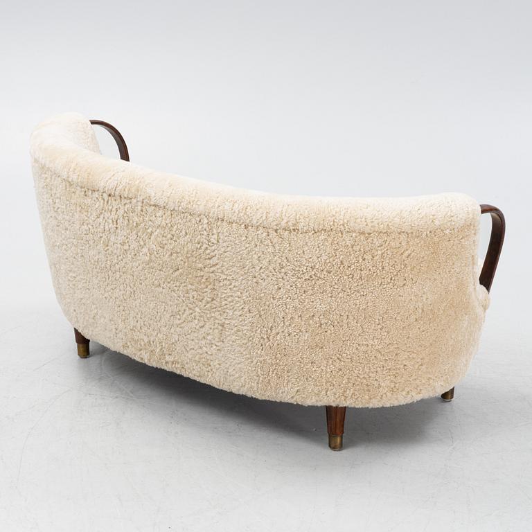 A curved sofa attributed to Viggo Boesen with new sheepskin upholstery and stained beech tree armrests.