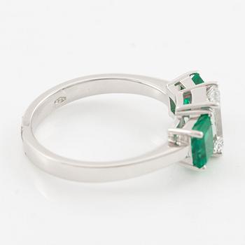 An 18K white gold ring set with an emerald-cut diamond and two step-cut emeralds.
