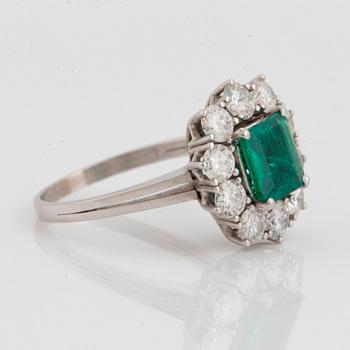 An 18K white gold ring set with a faceted emerald ca 1.15 cts and round brilliant-cut diamonds.