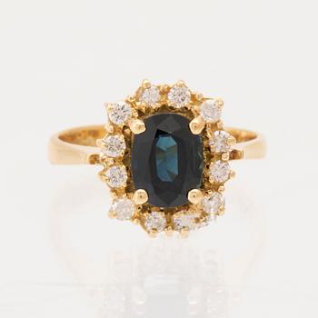 An 18K yellow gold ring set with an oval-cut sapphire and round brilliant-cut diamonds.