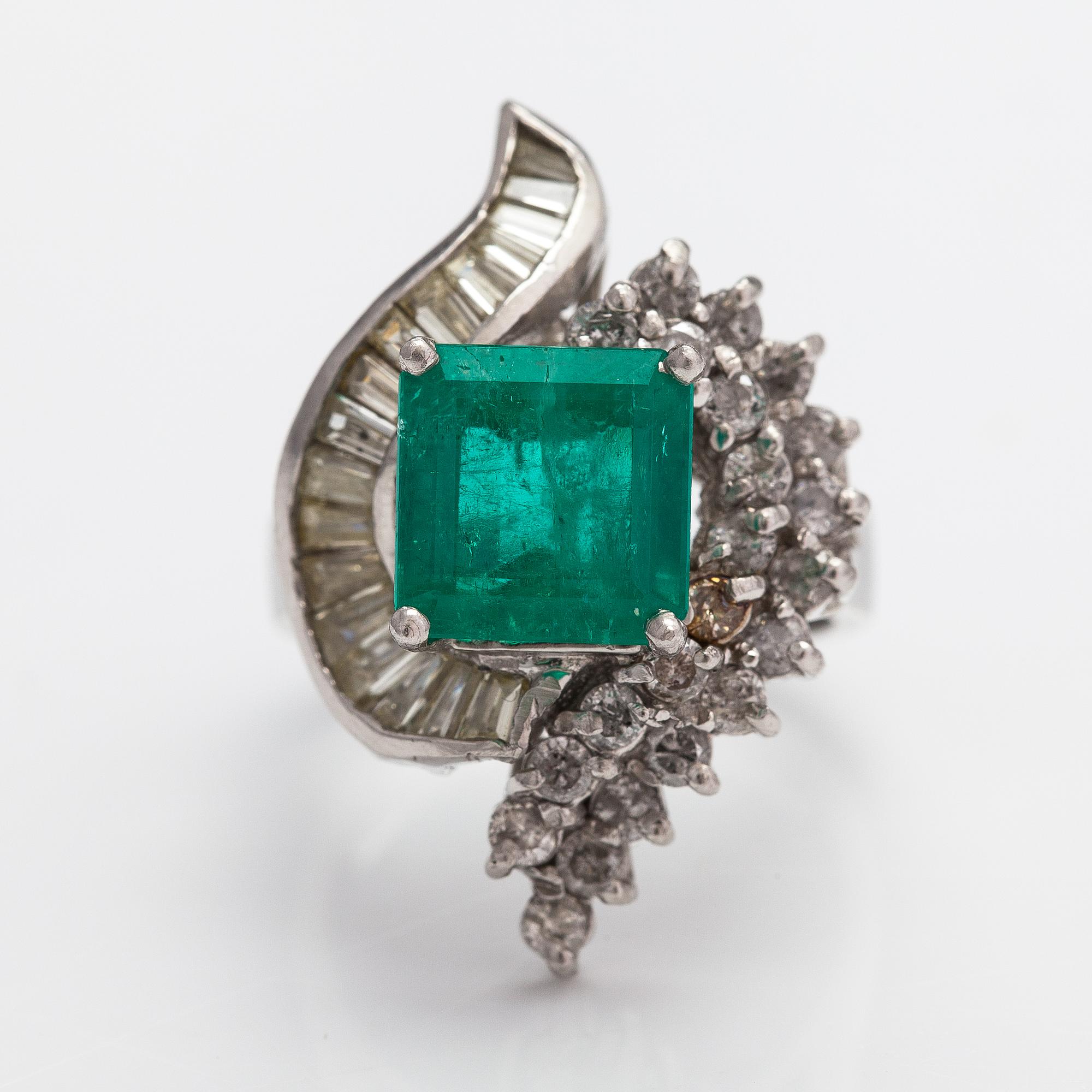A platinum ring with a ca. 3.20 ct emerald and diamonds ca. 1.16 ct in total.