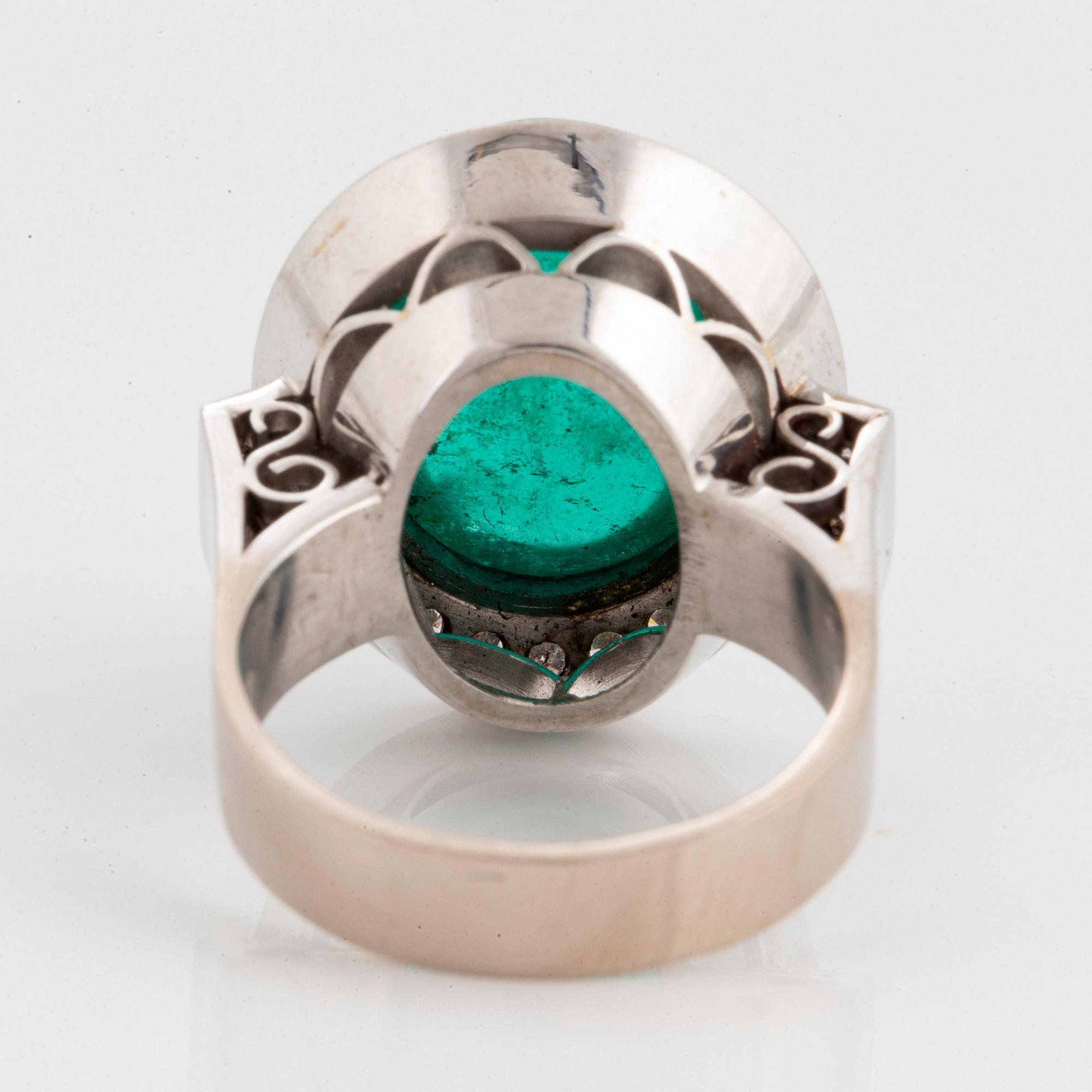 An 18K white gold ring set with a cabochon-cut emerald and round brilliant-cut diamonds.