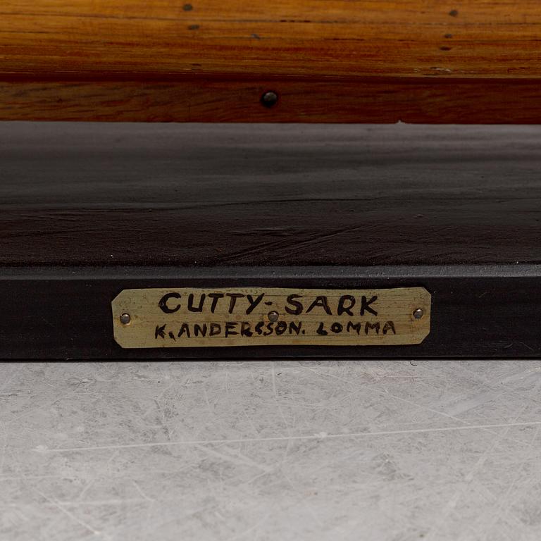 A wooden scale model of Cutty Sark on a painted wooden stand.