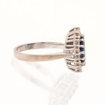 An 18K white gold ring set with an oval faceted sapphire and round brilliant-cut diamonds.