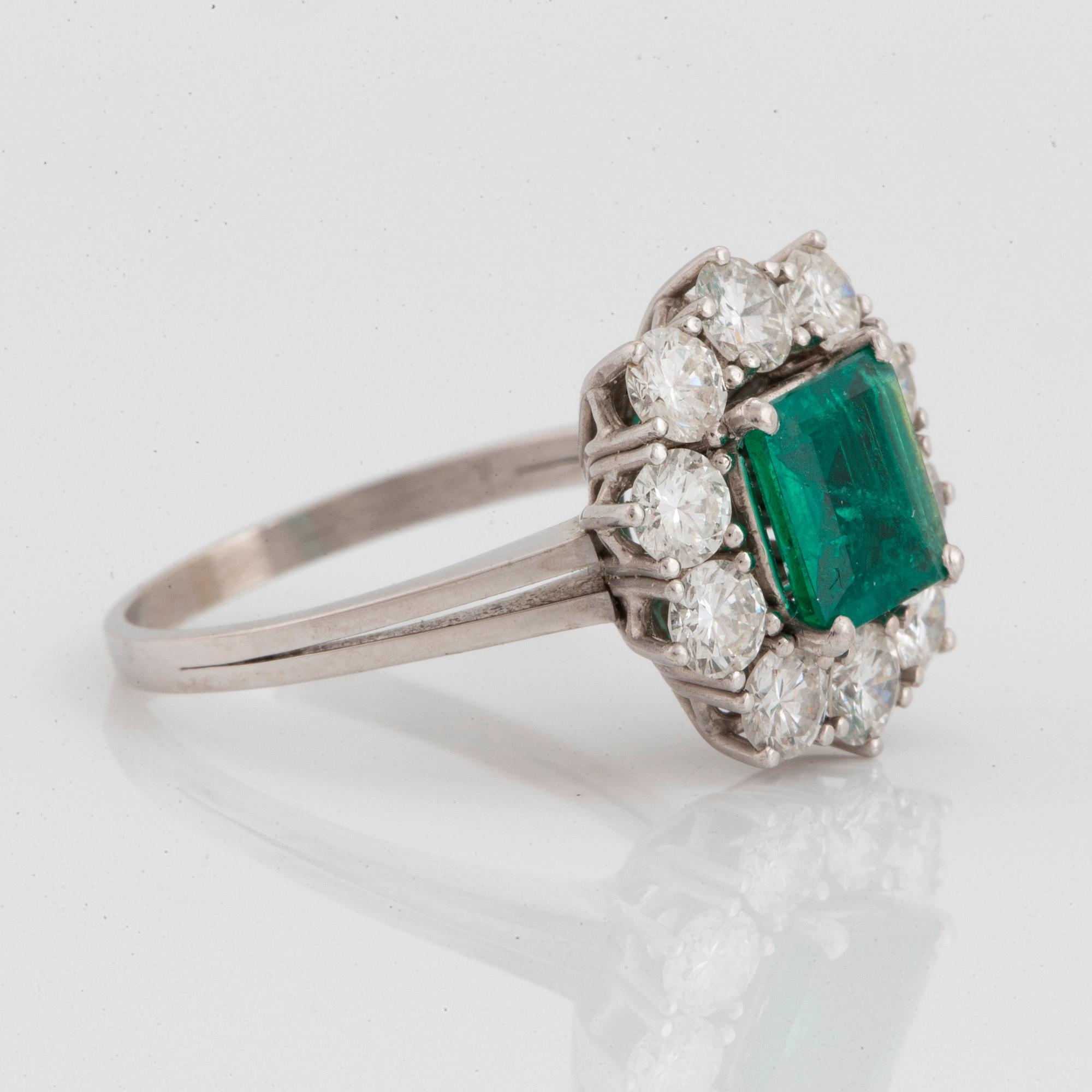 An 18K white gold ring set with a faceted emerald ca 1.15 cts and round brilliant-cut diamonds.