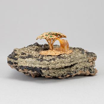 A sculpture of an agate elephant under a gilt three with inlays of tsavorites on rock formation, unmarked, 20th Century.