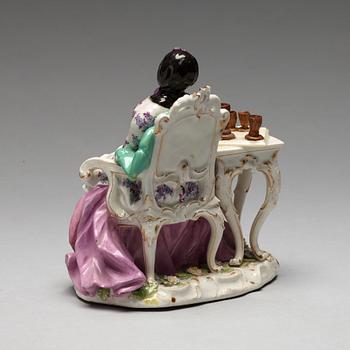 A Meissen porcelain figure of a lady by a table.