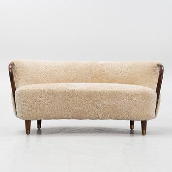 A curved sofa attributed to Viggo Boesen with new sheepskin upholstery and stained beech tree armrests.