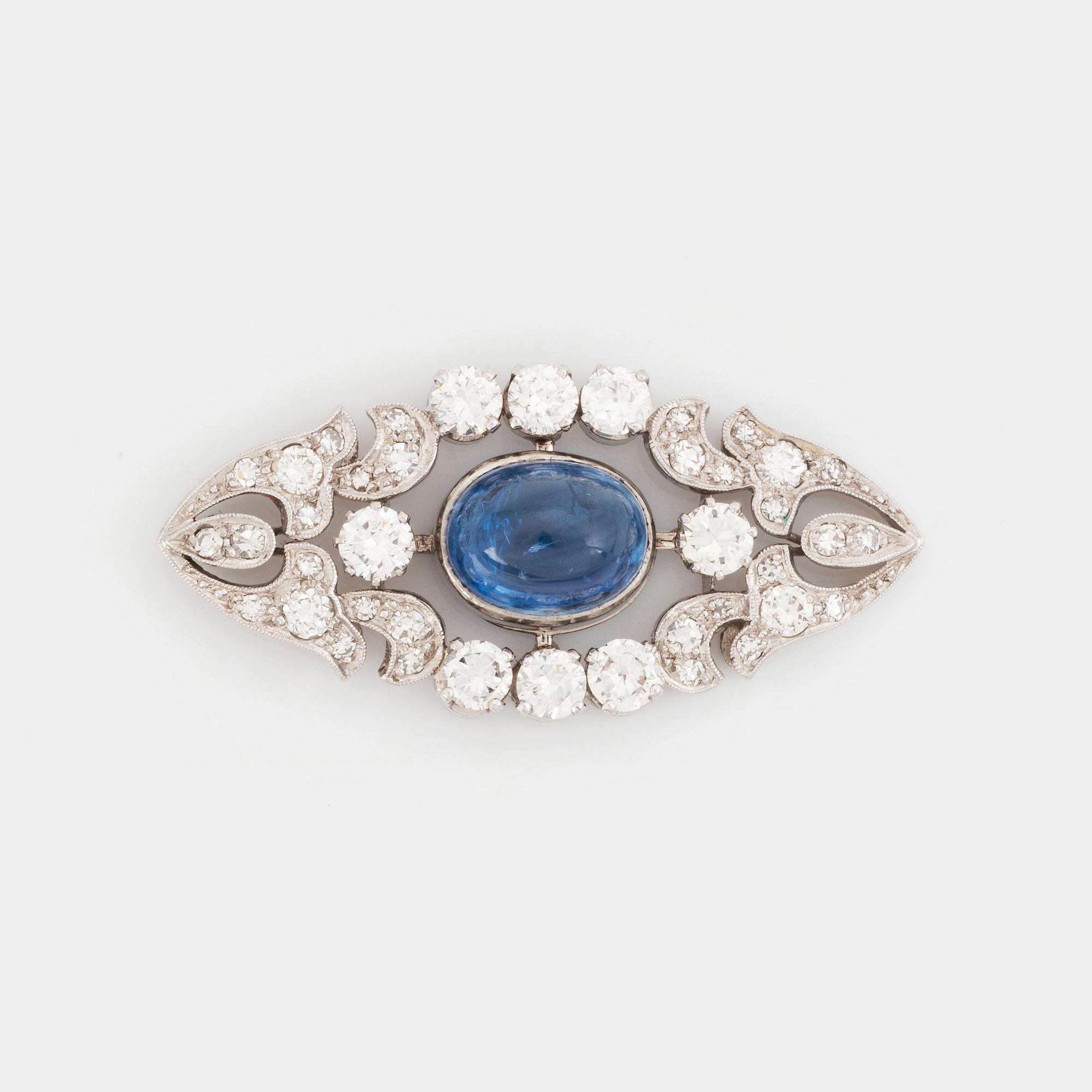 A platinum brooch set with a cabochon-cut sapphire and a cabochon-cut emerald.