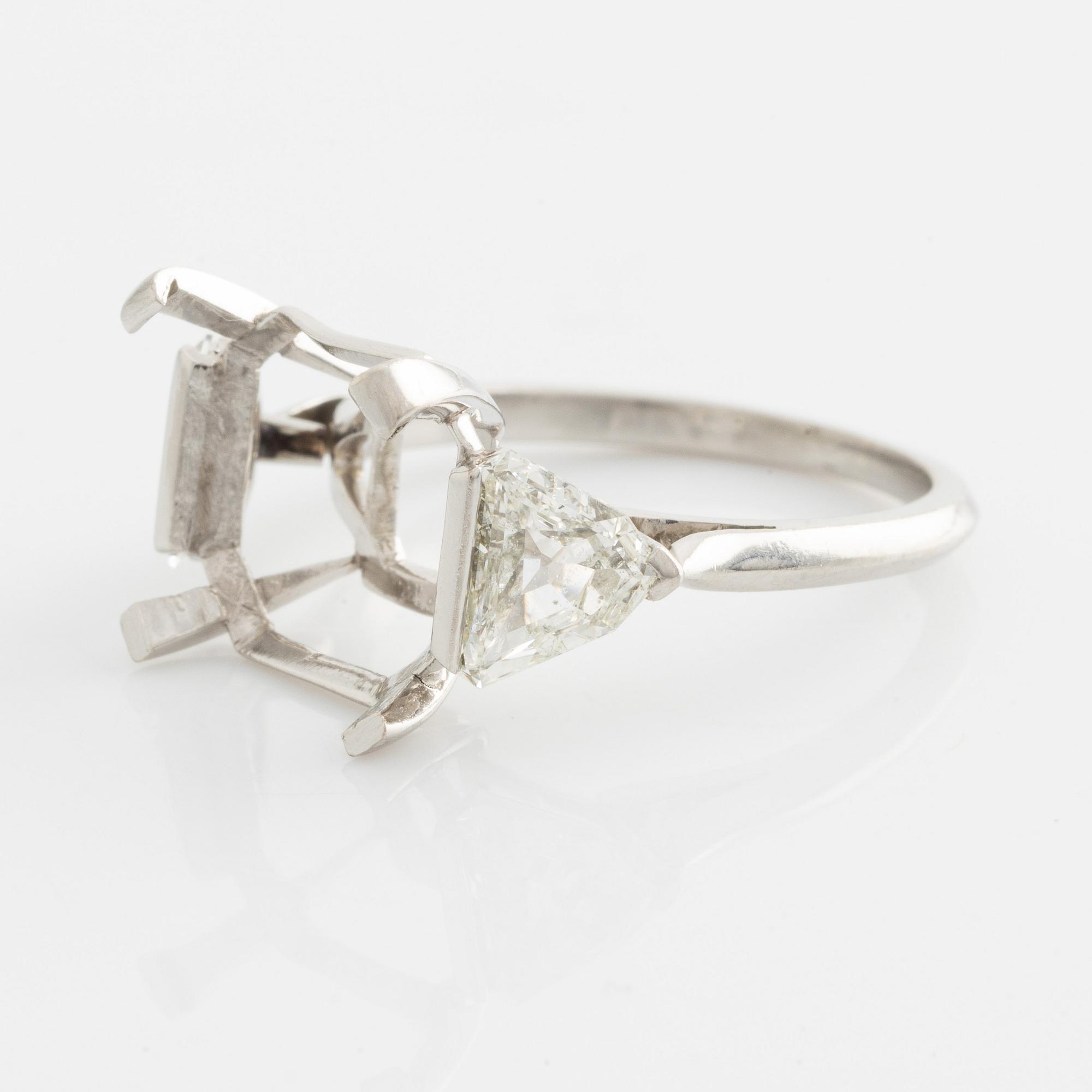 A platinum ring with and empty setting and with two triangular step cut diamonds.