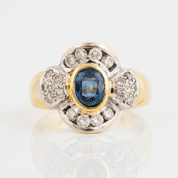 An 18K gold ring set with a synthetic sapphire and round brilliant-cut diamonds.