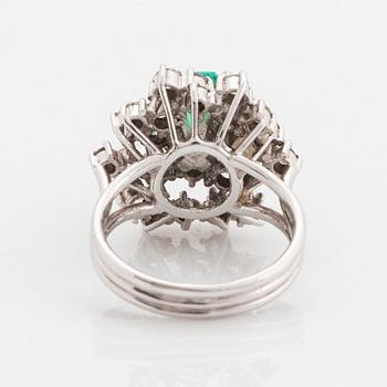 A platinum ring set with a faceted emerald and round brilliant-cut diamonds.