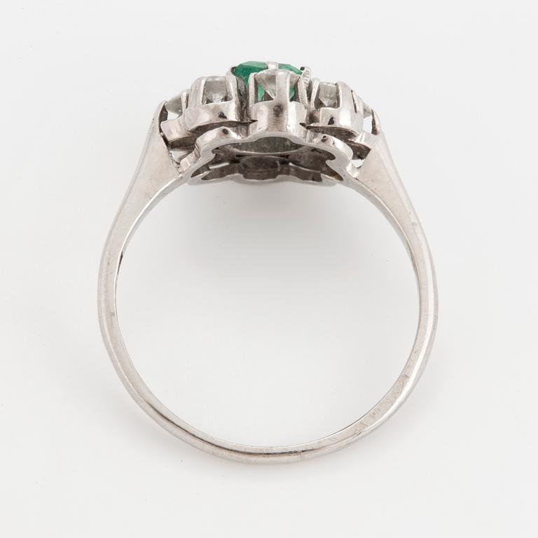 A ring set with a faceted emerald and round brilliant-cut diamonds.