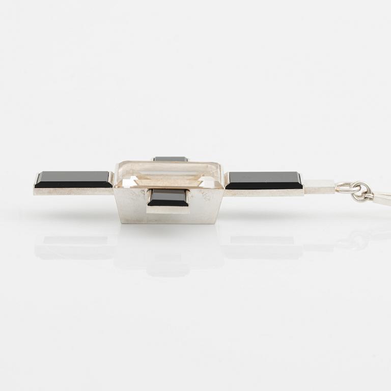 Wiwen Nilsson, hängsmycke i form av ett kors i sterlingsilver med fasettslipad bergkristall och onyx, Lund 1939.