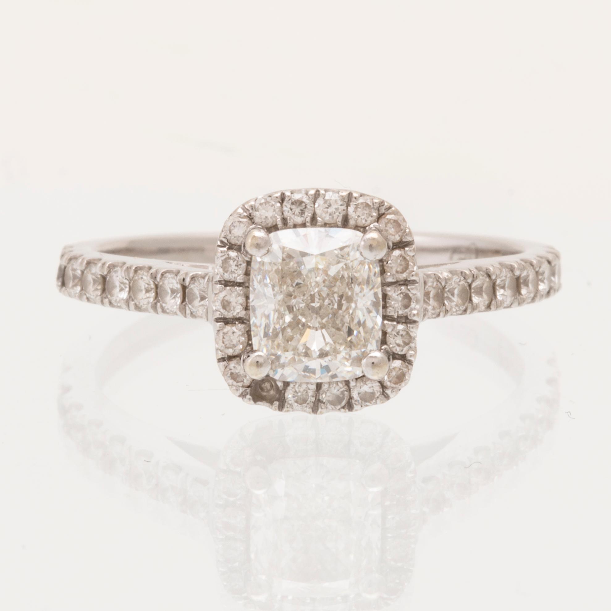 An 18K white gold ring set with a modified cushion-cut diamond and round brilliant-cut diamonds.