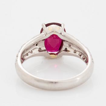 A platinum ring set with a faceted ruby and round brilliant-cut diamonds.