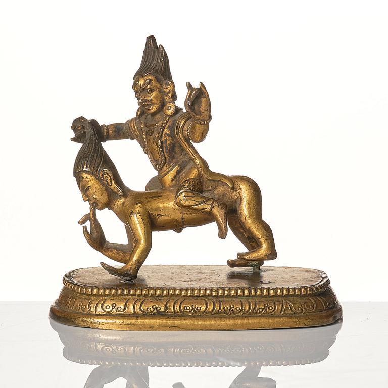 A small gilt bronze figure wrathful deity riding on a corpse, Tibeto-Chinese, 18th Century.