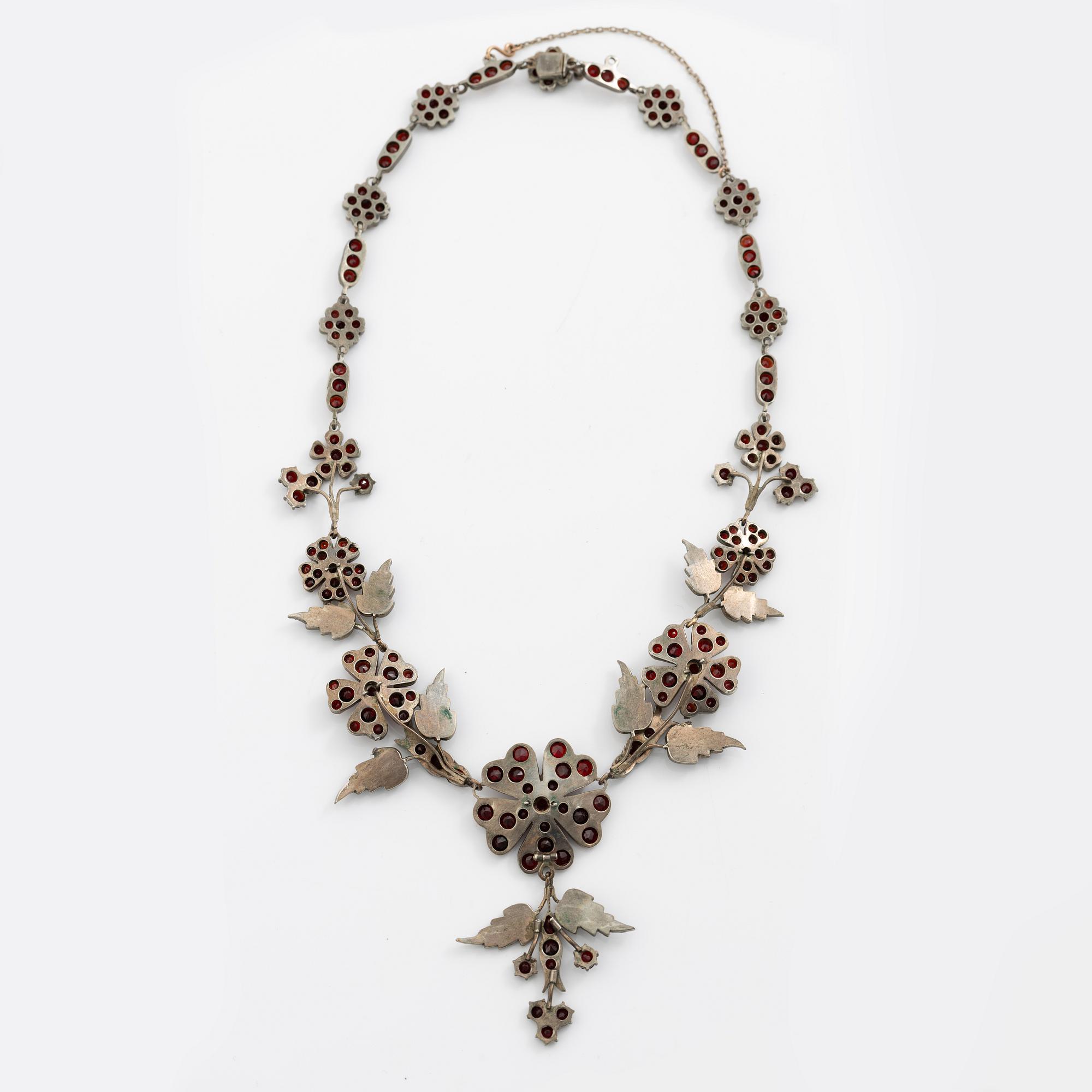 Garniture, necklace/bracelet and earrings in silver with garnets in the form of floral motifs, around the turn of the 20th century.