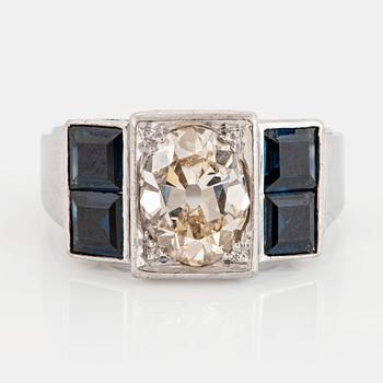 1074. An 18K white gold ring set with an old-cut dimond weight ca 1.50 cts and step-cut sapphires.
