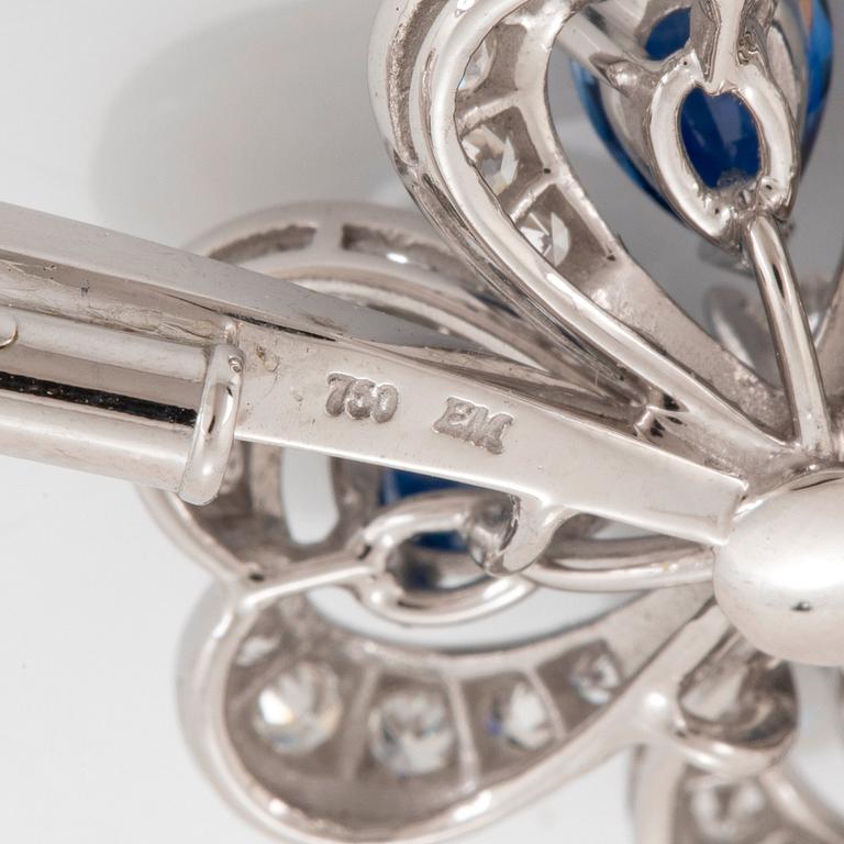 A Meister brooch in 18K white gold set with faceted sapphires, a round brilliant-cut diamond.