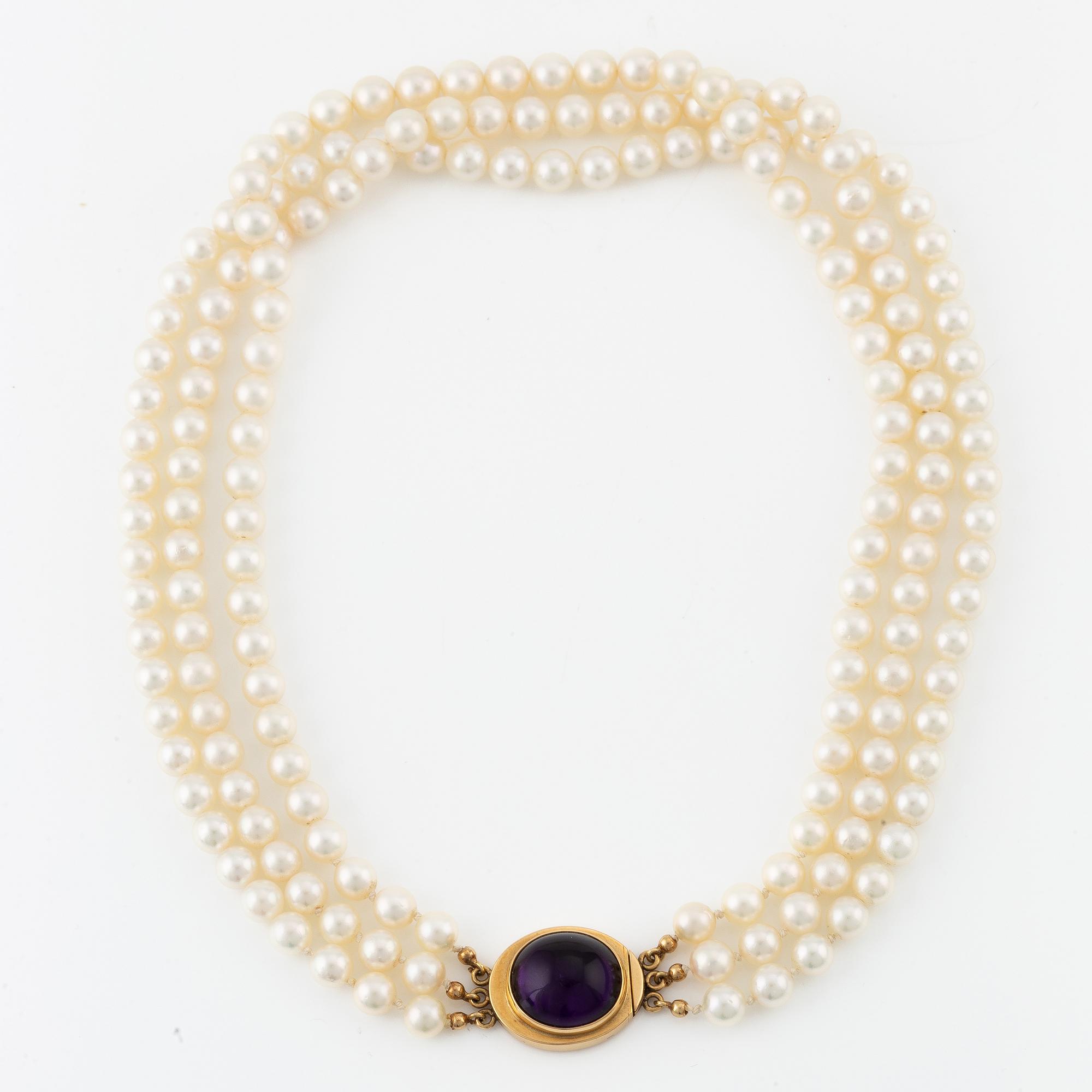 A three strand cultured pearls neckace clasp 18K gold with a purple stone, likely amethyst.
