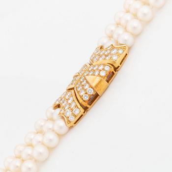 A Cartier triple strand cultured pearl necklace with an 18K gold clasp set with round brilliant-cut diamonds.