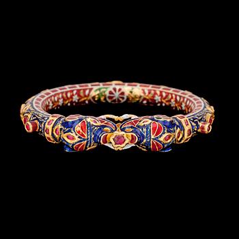 1023. A cabochon cut ruby- and gold bangle with blue and red enamel, India, late 19th century.
