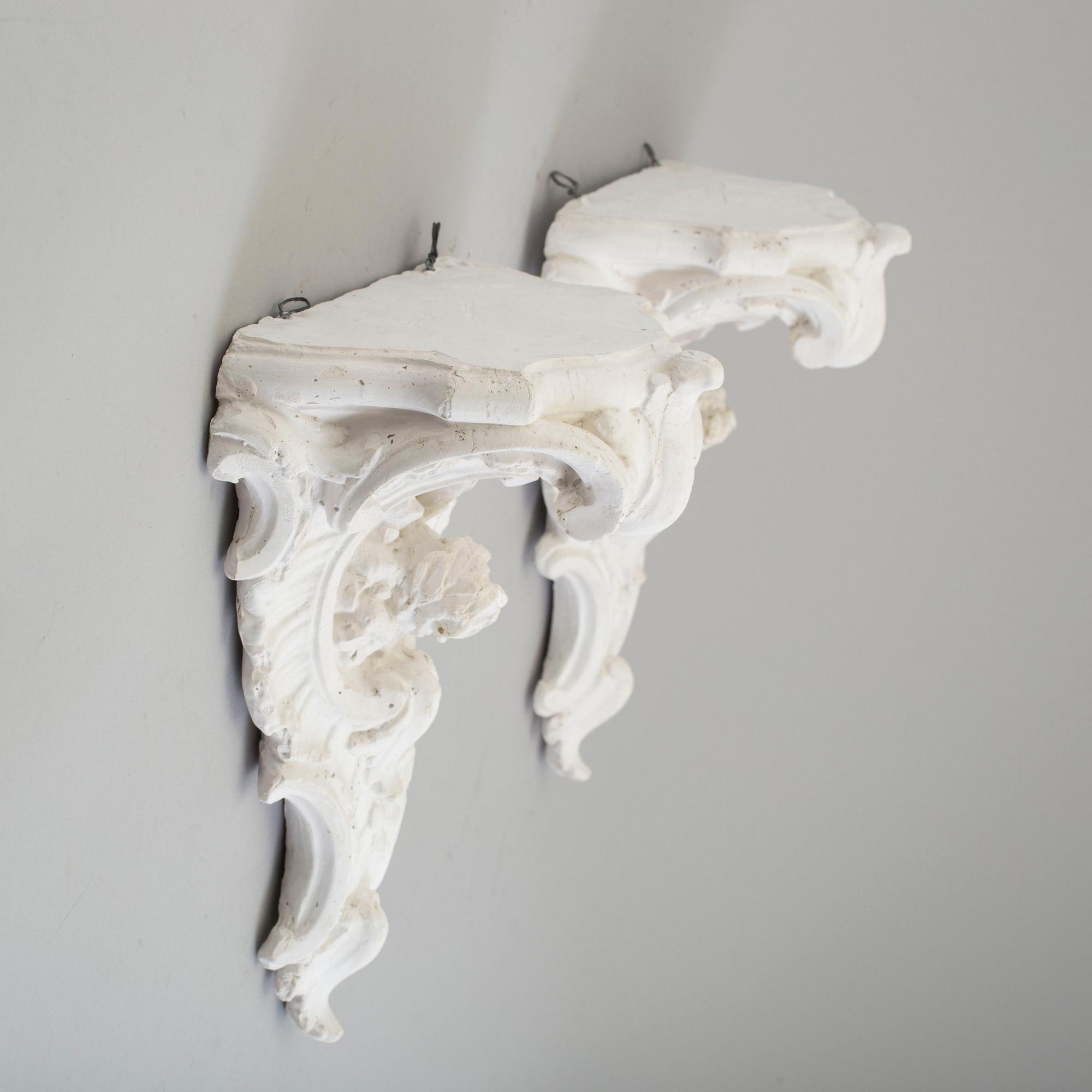 A pair of consoles and a set of three decor-elements, plaster, 20th century.