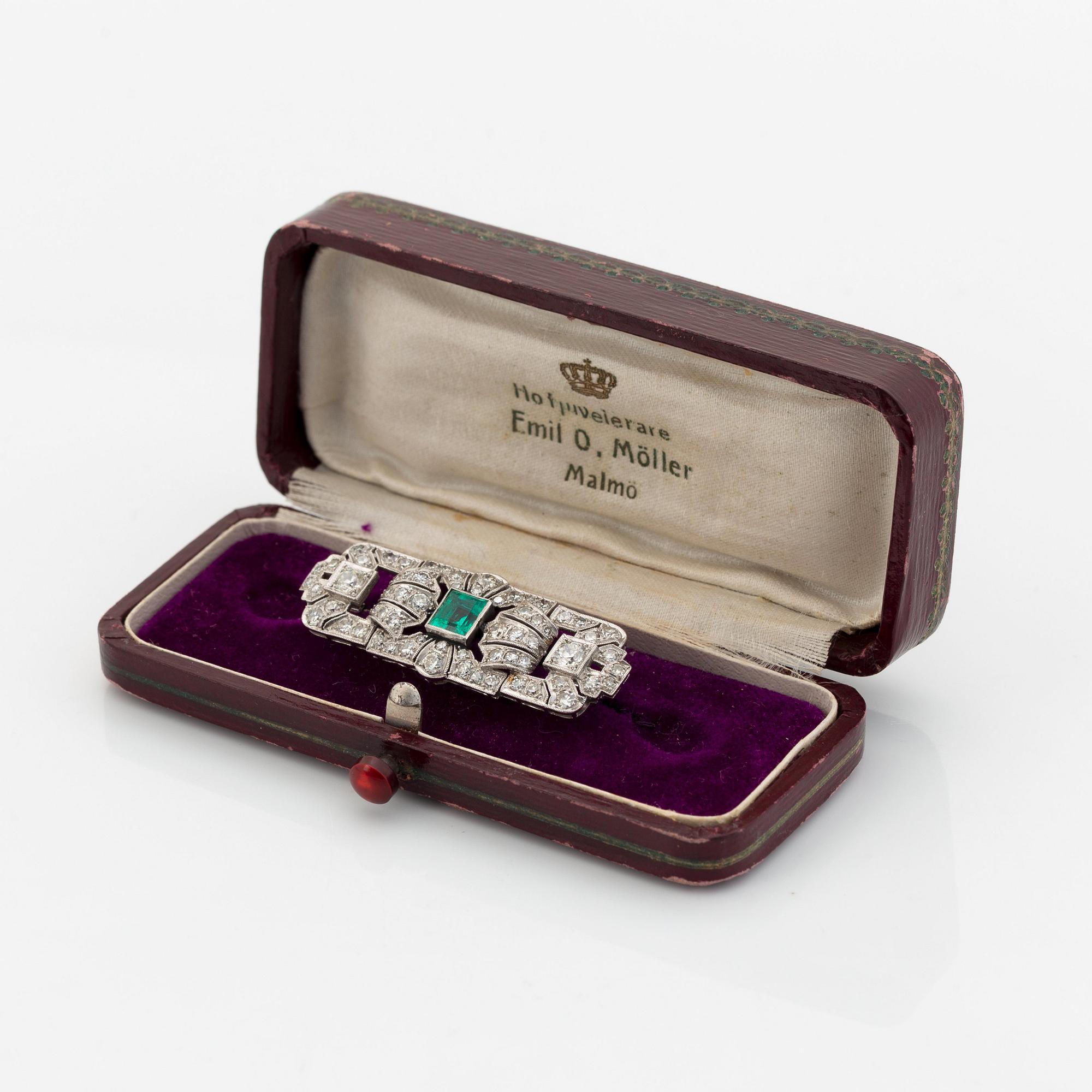 A platinum brooch set with a step-cut emerald and old- and eight-cut diamonds.