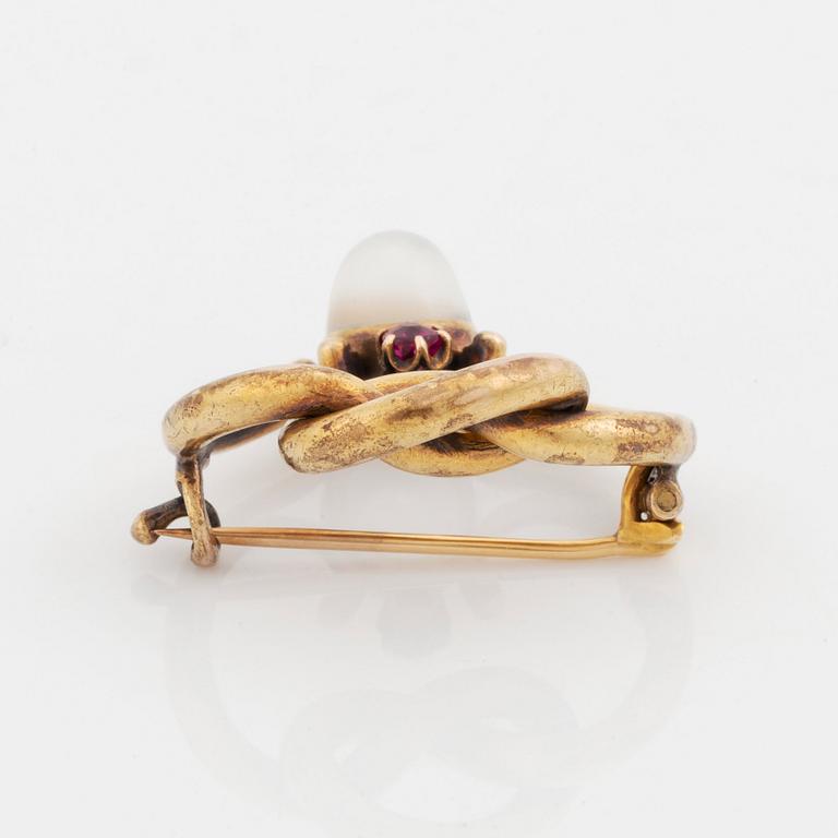 A 14K gold brooch set with a cabochon-cut moonstone and a pink sapphire.