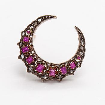 A cresent moon brooch made of 14K gold, silver, rubies and diamonds.