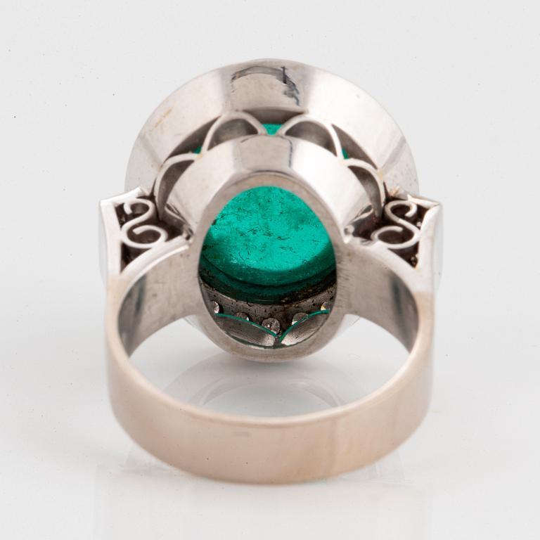 An 18K white gold ring set with a cabochon-cut emerald and round brilliant-cut diamonds.