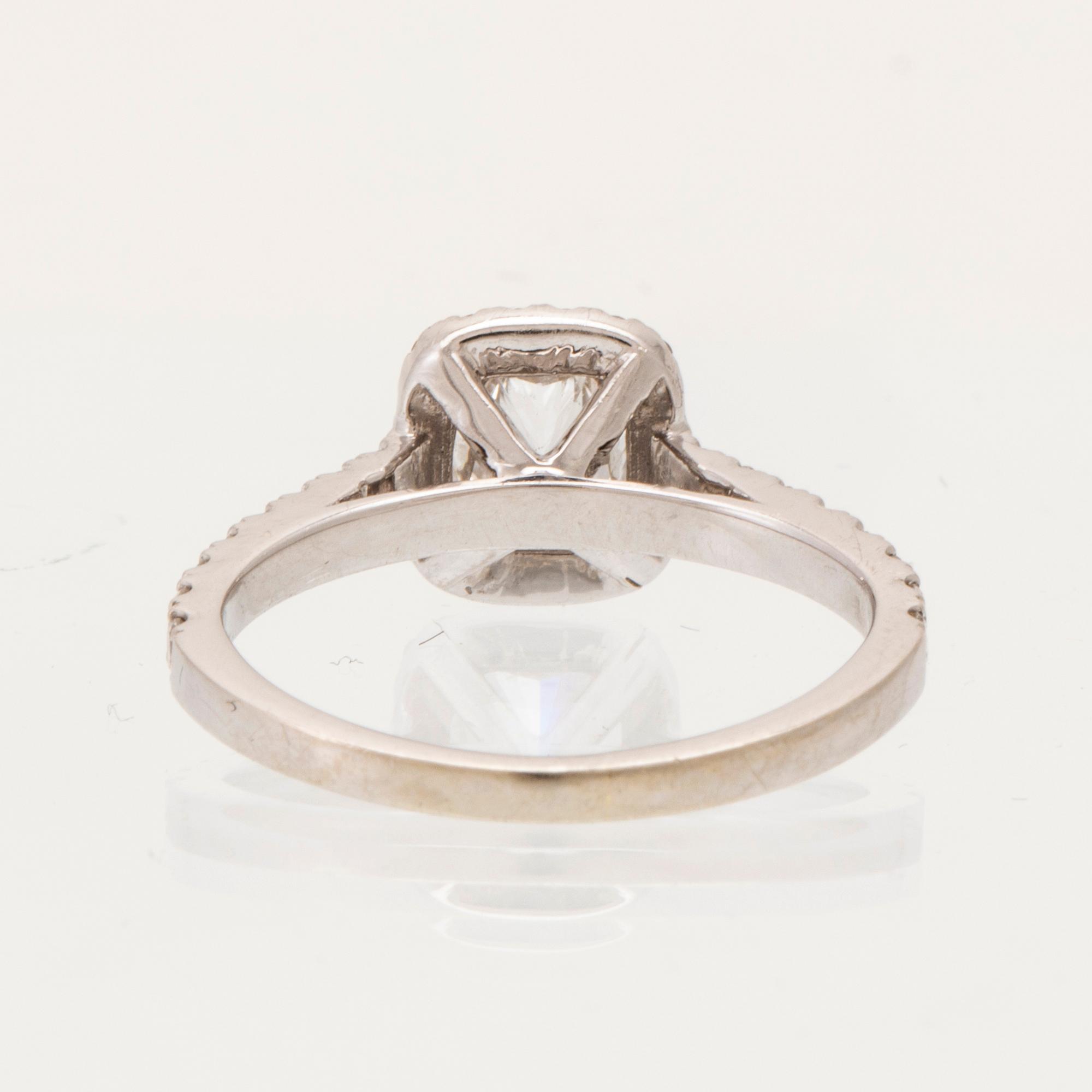 An 18K white gold ring set with a modified cushion-cut diamond and round brilliant-cut diamonds.