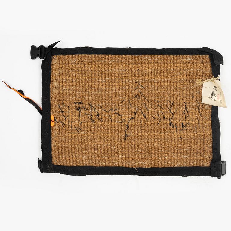 Banksy, dörrmatta, handbroderad med material från livvästar, 2019.