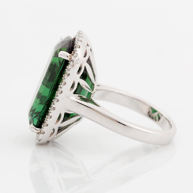 An 18K white gold ring set with a faceted green tourmaline and round brilliant-cut diamonds.