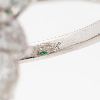 An platinum ring set with a faceted emerald and brilliant-cut pearshaped diamonds.