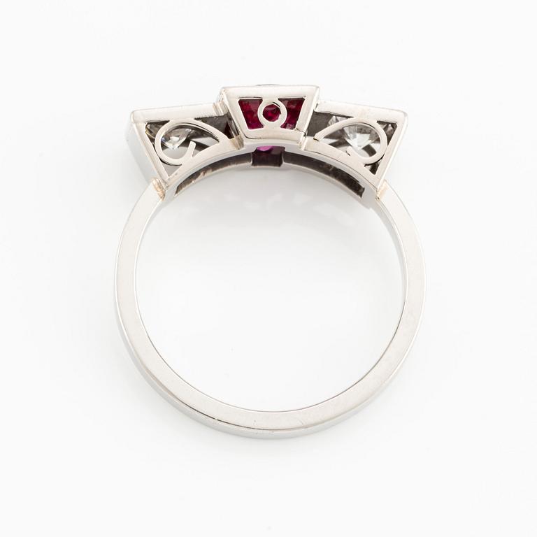 A platinum ring with a faceted ruby and two round brilliant-cut diamonds.