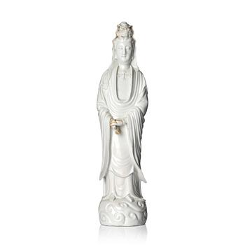 A blanc-de-chine figure of Guanyin, Qing dynasty. Modelled standing above crested waves, wearing a long veil...