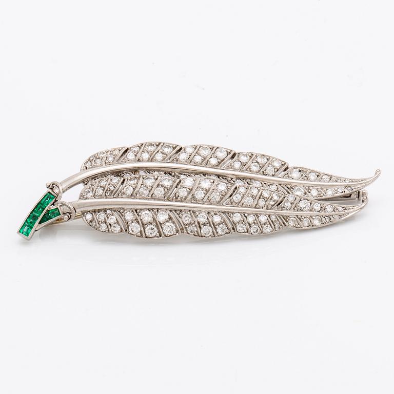 A platinum brooch set with round brilliant-cut diamonds and emeralds.