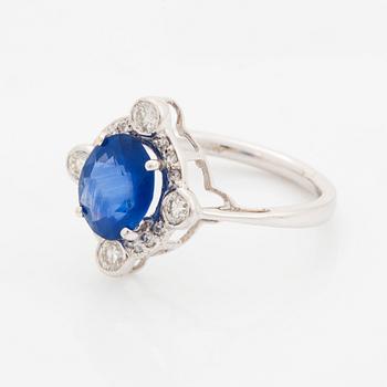 An 18K white gold ring set with a faceted sapphire and round brilliant-cut diamonds.