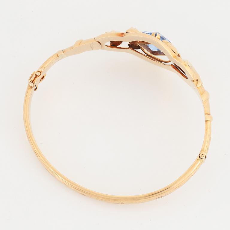 An 18K gold bangle set with a blue synthetic stone.