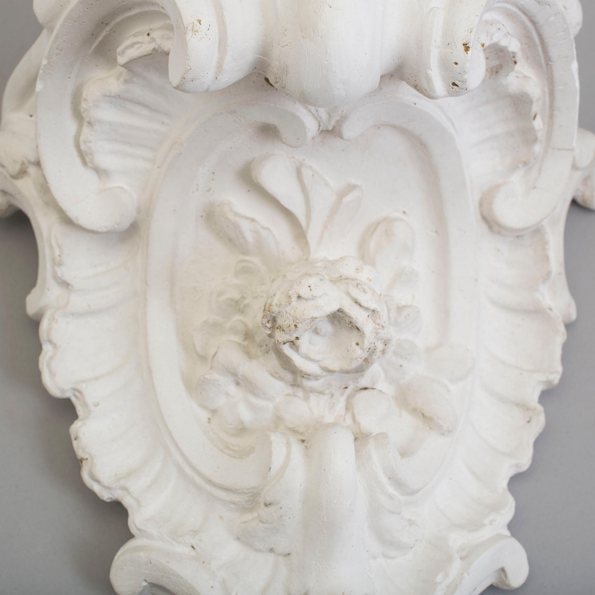 A pair of consoles and a set of three decor-elements, plaster, 20th century.