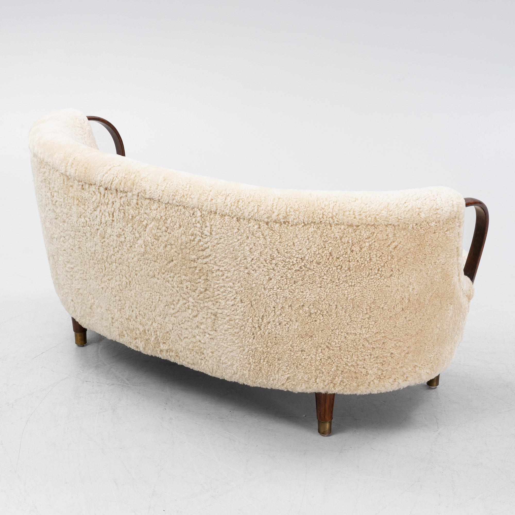A curved sofa attributed to Viggo Boesen with new sheepskin upholstery and stained beech tree armrests.