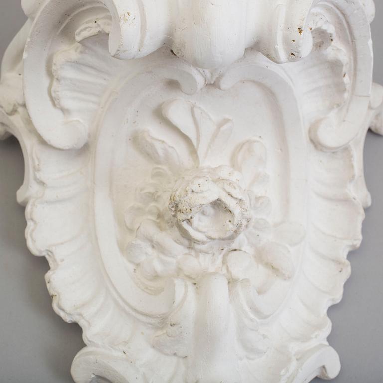 A pair of consoles and a set of three decor-elements, plaster, 20th century.