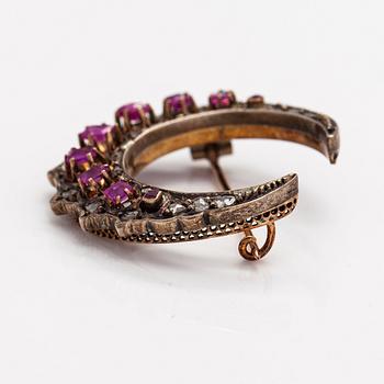 A cresent moon brooch made of 14K gold, silver, rubies and diamonds.
